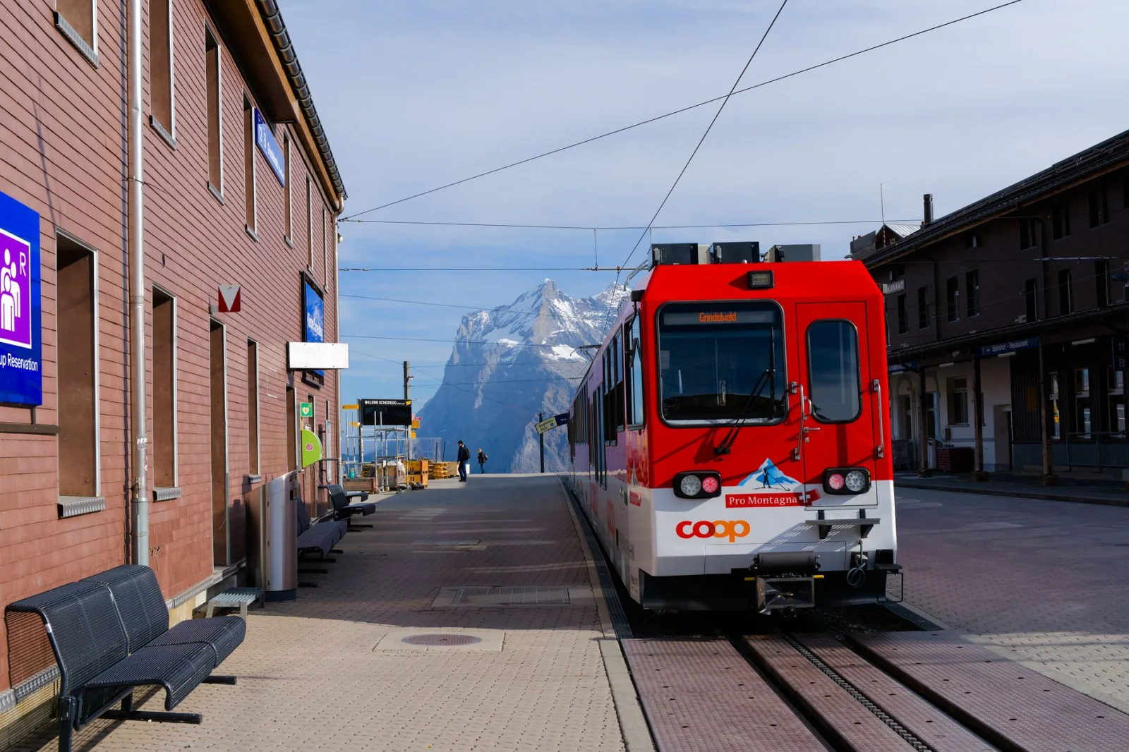 Red mountain train at an Alpine station platform with a snow-capped peak behind it