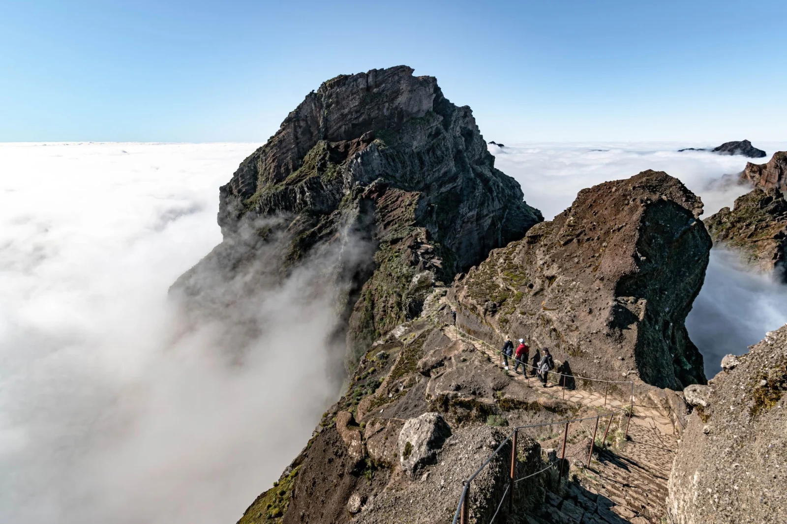 Hikers walking toward Pico Ruivo above clouds in Madeira’s central mountains.