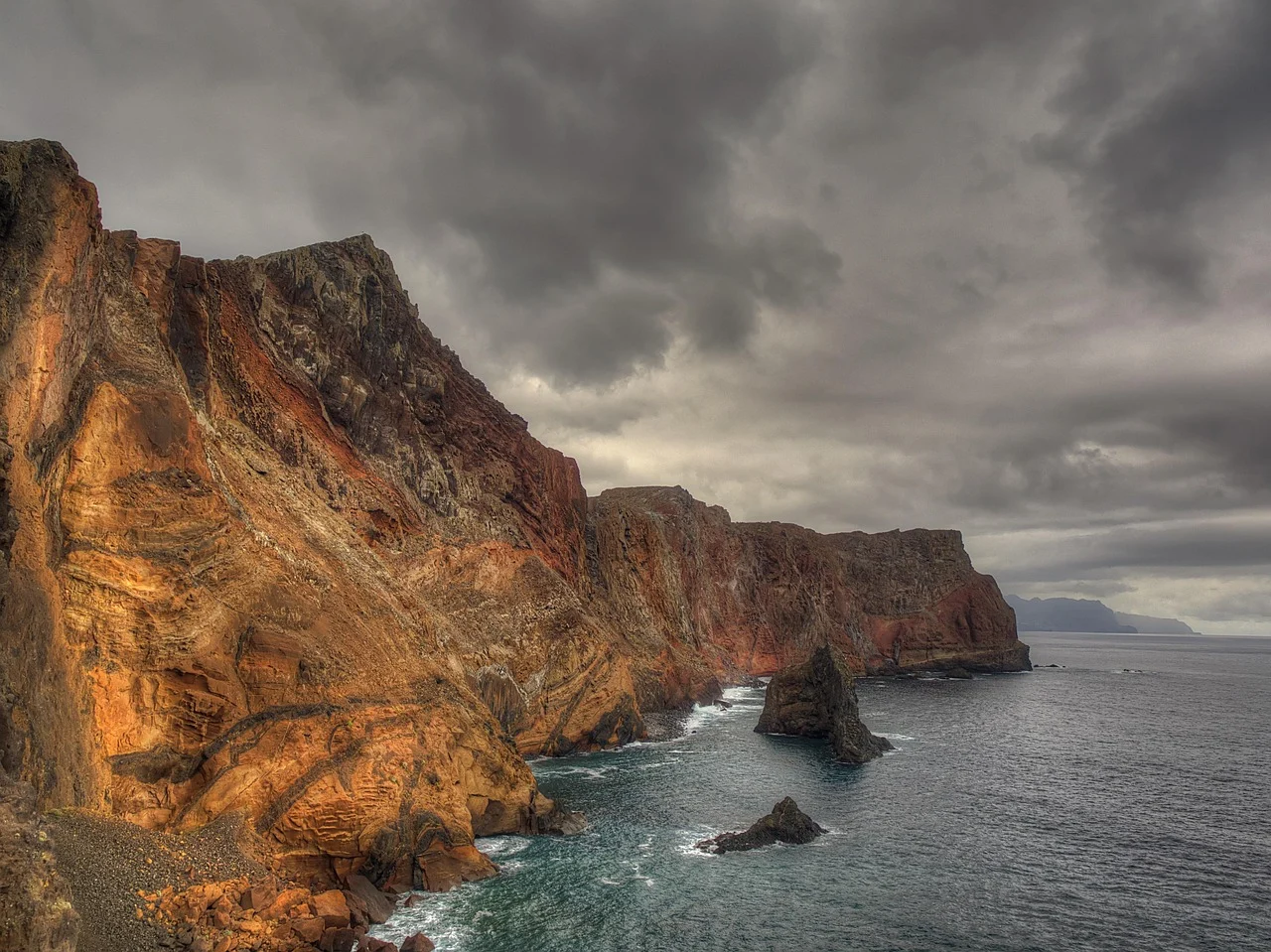 Hiker on the Ponta de São Lourenço trail with volcanic cliffs and the Atlantic Ocean.