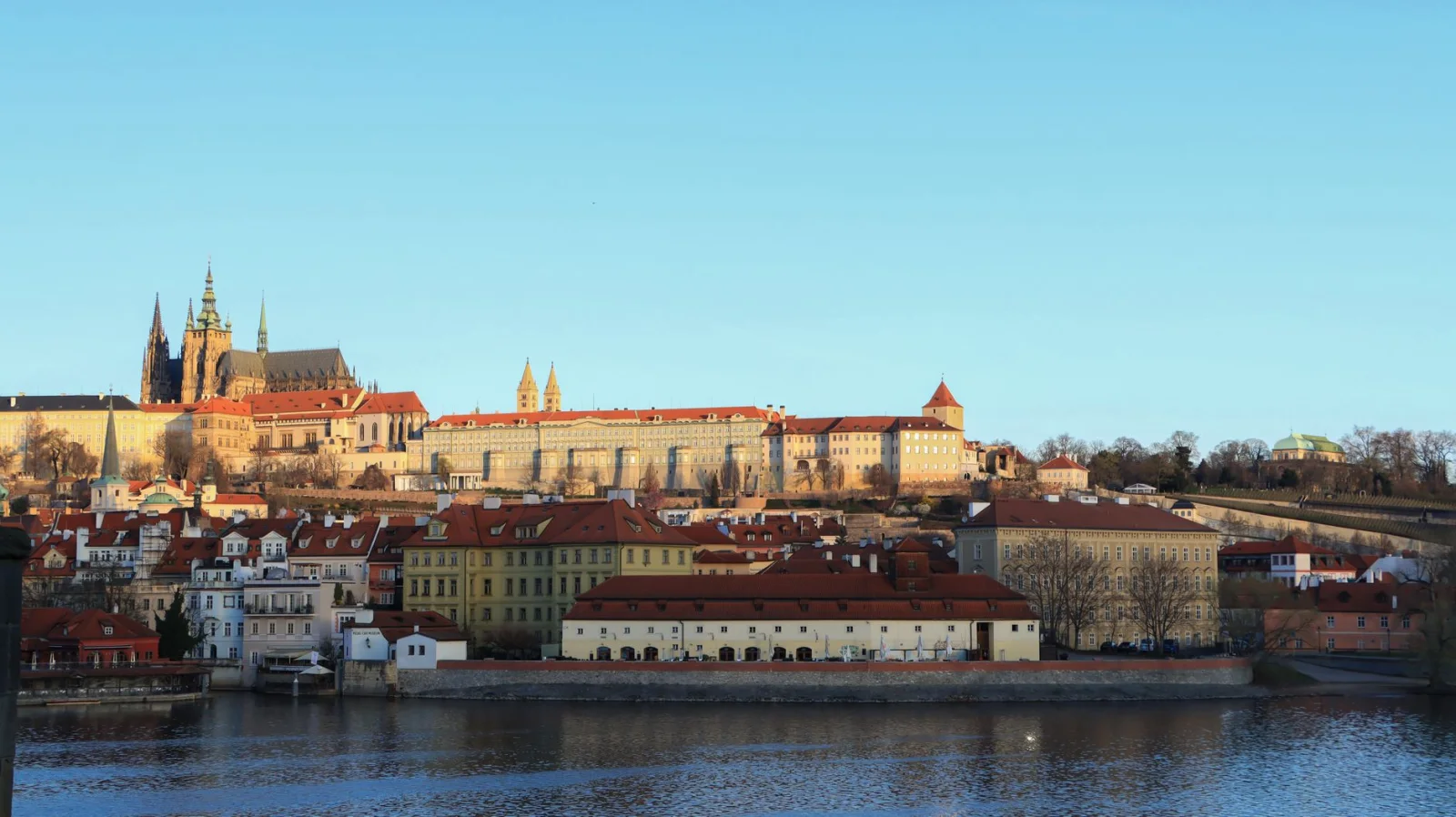 Prague Castle and red rooftops seen across the Vltava River at golden hour